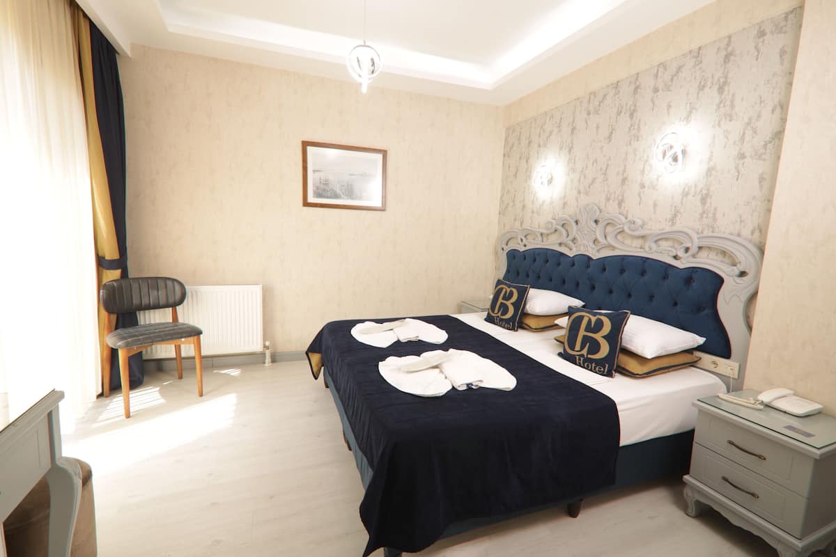 A hotel room with a large bed, a nightstand, a chair, a radiator, and a framed picture on the wall.