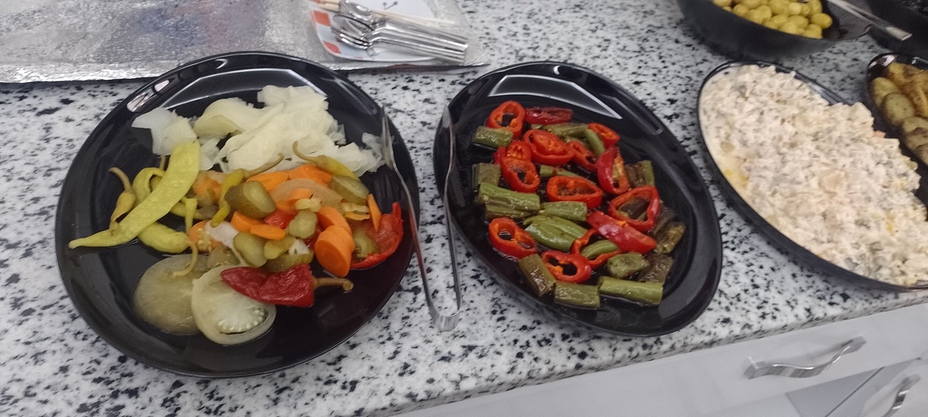 Two black plates with sliced vegetables on a granite countertop.
