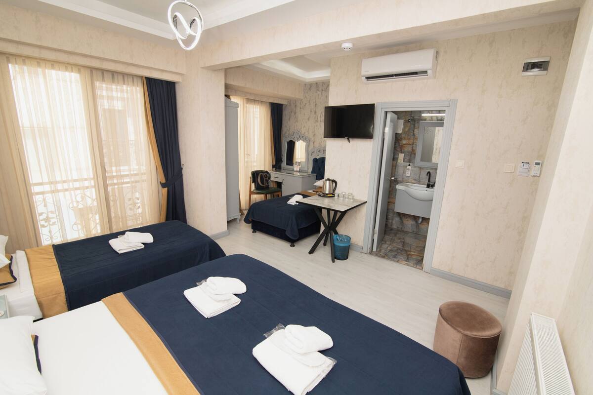 A hotel room with two beds, a desk, a chair, a TV, a bathroom, and a trash bin.