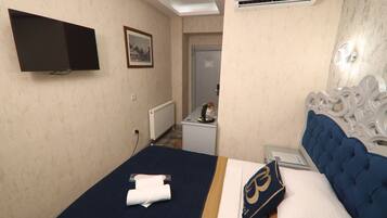 A hotel room with a bed, a flat-screen TV mounted on the wall, a small table with a coffee maker, and a door leading to a bathroom.