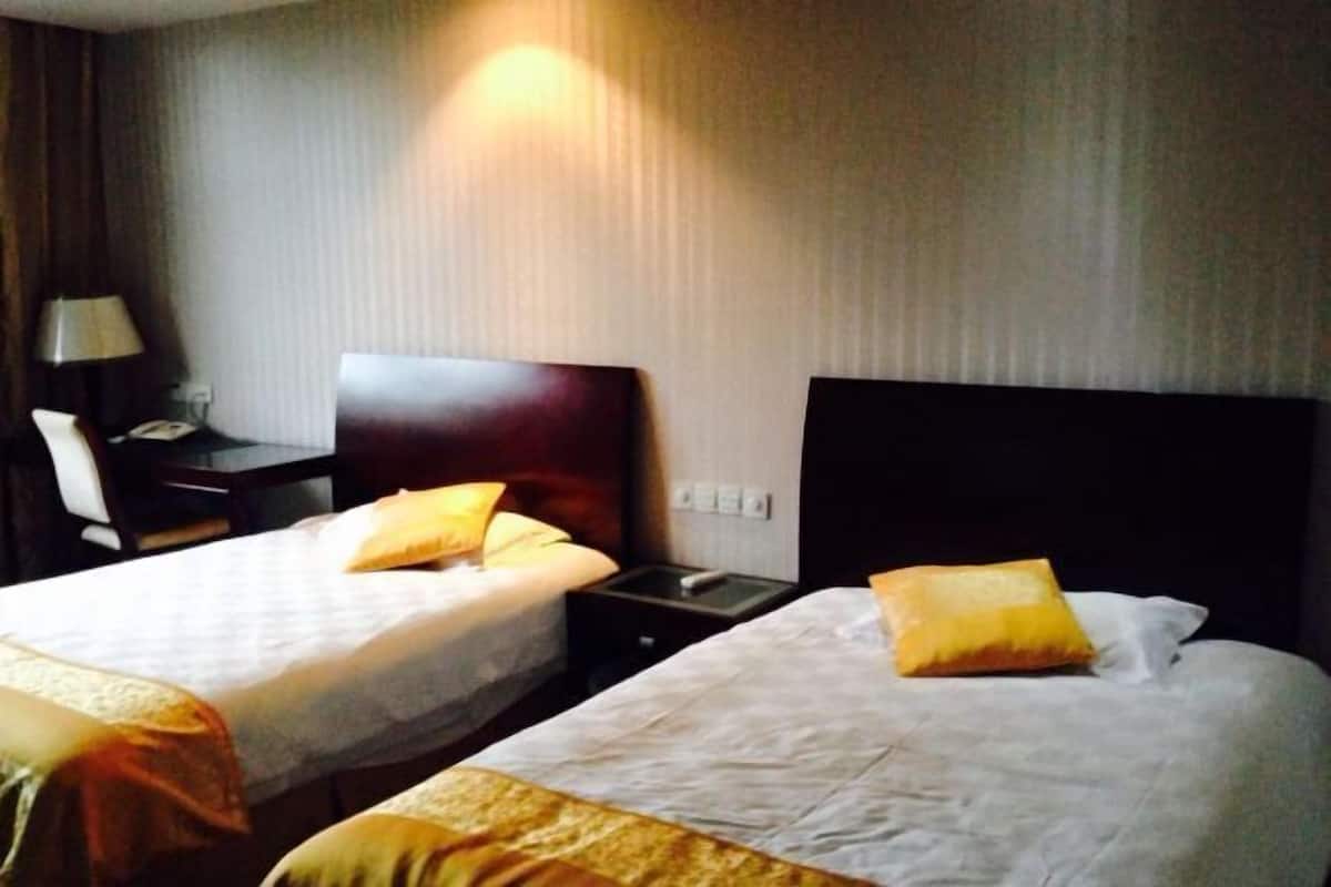 Two beds with white linens and yellow pillows, a bedside table with a lamp, and a wall-mounted light fixture.