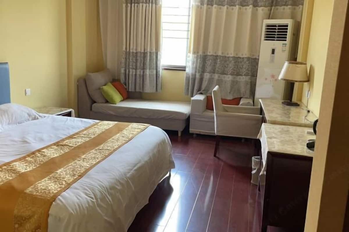 A hotel room with two beds, a sofa, a desk, and an air conditioning unit.