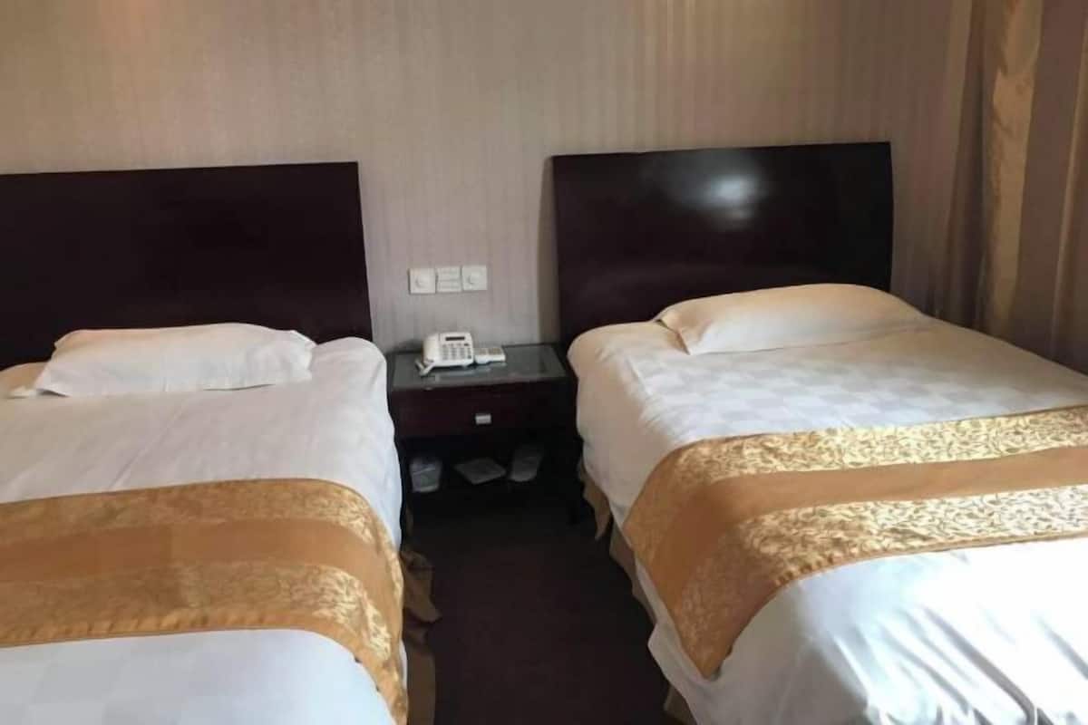 A hotel room with two beds, each with a headboard, a bedside table with a phone, and a carpeted floor.