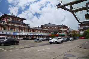 A parking lot with several cars, a building with traditional architecture, and a clear sky. - Xintiandi Hotel (Haiyan)