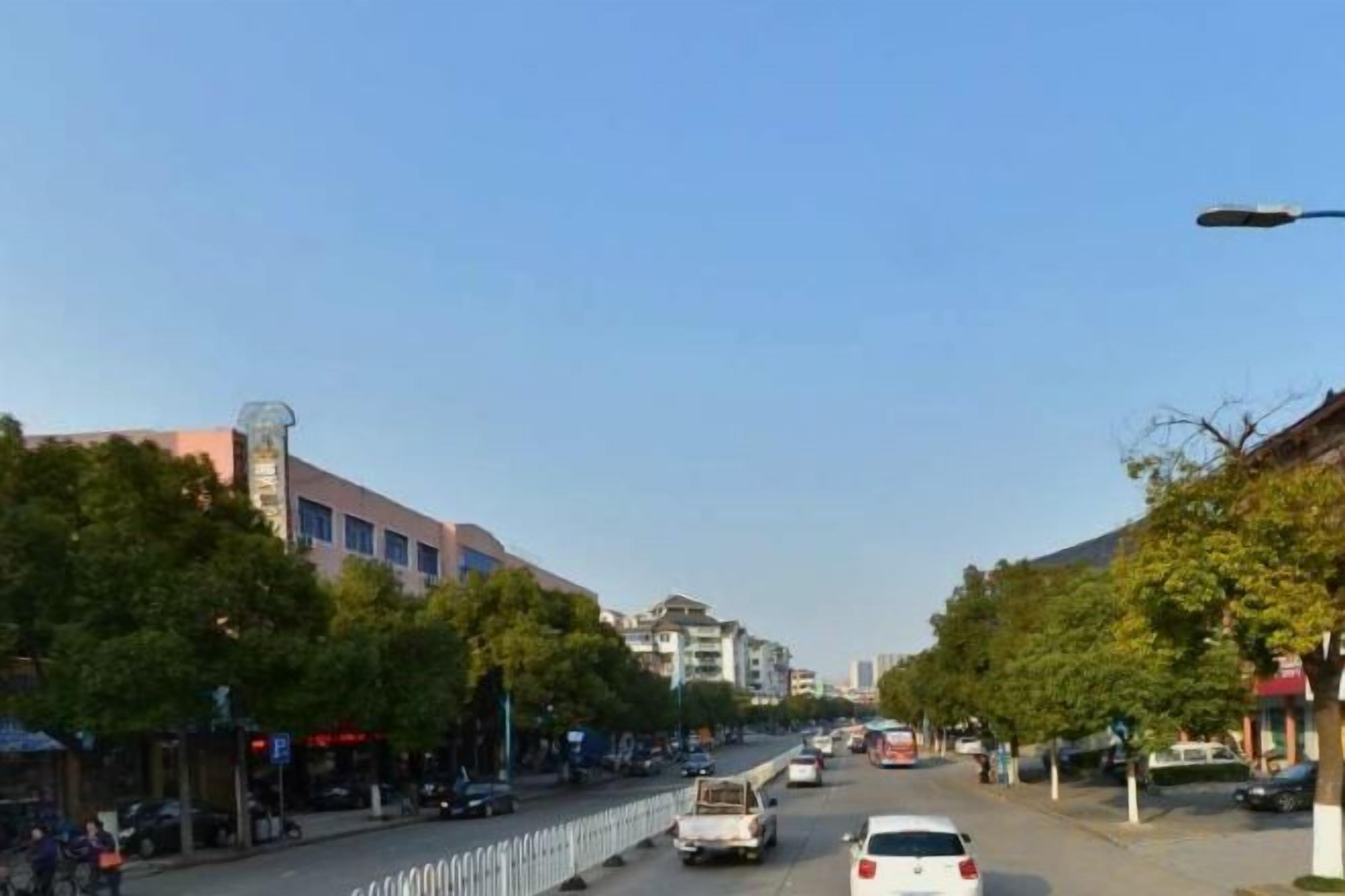 A street view with buildings, trees, and parked cars.