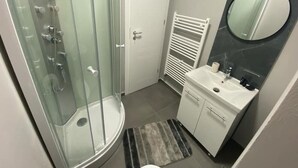 Un baño con ducha compartimentada con vidrio, un lavamanos blanco con espejo y un perchero para toallas.