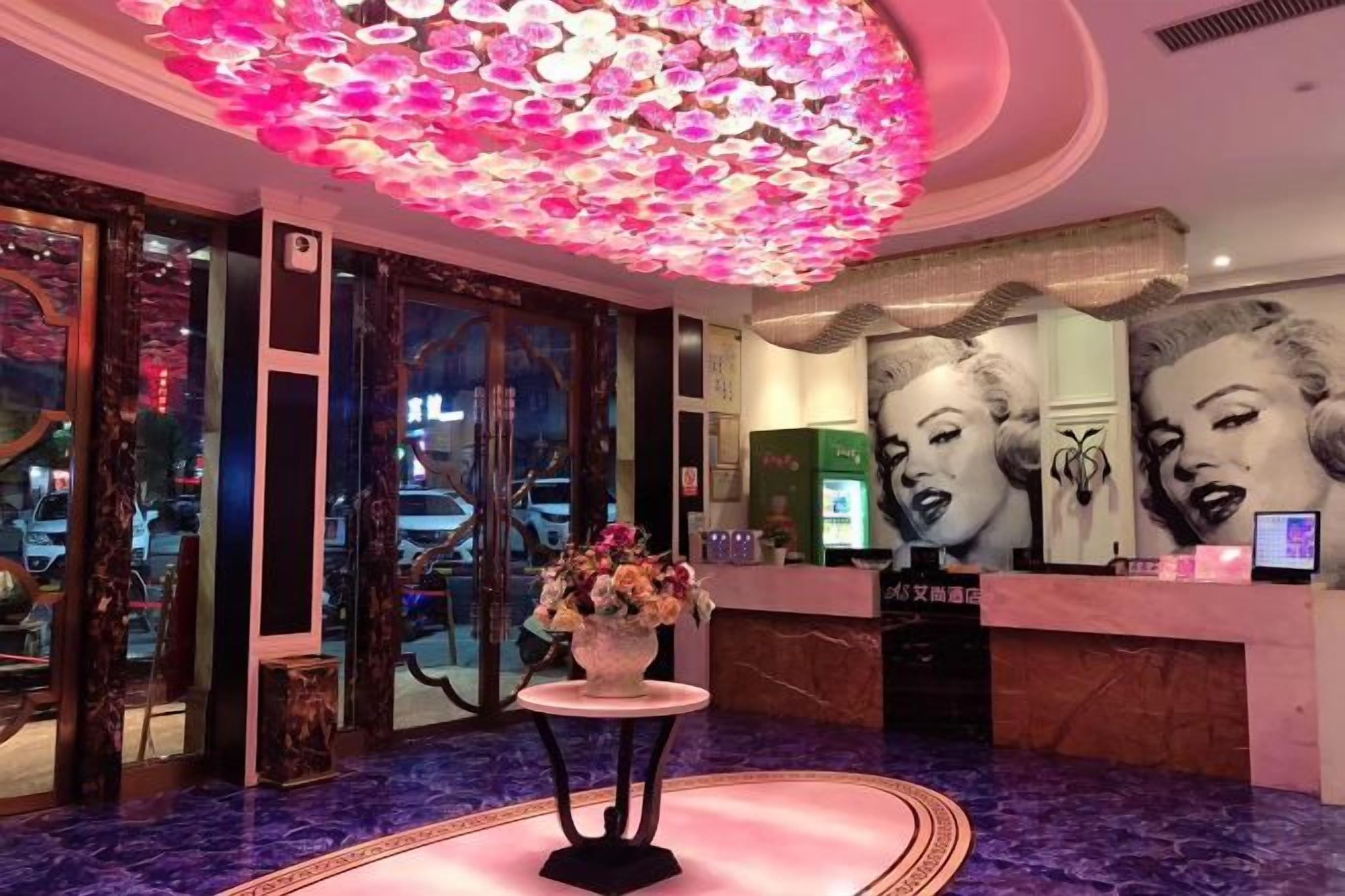 A lobby with a reception desk, a vase of flowers, and a ceiling with a floral light fixture.