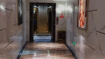 A hallway with a marble floor leading to a door, framed by walls with a patterned wallpaper and a poster.