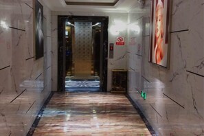 A hallway with a marble floor leading to a door, framed by walls with a patterned wallpaper and a poster. - Aishang Hotel (Pubei Maoyuan Diwang International) (Pubei)