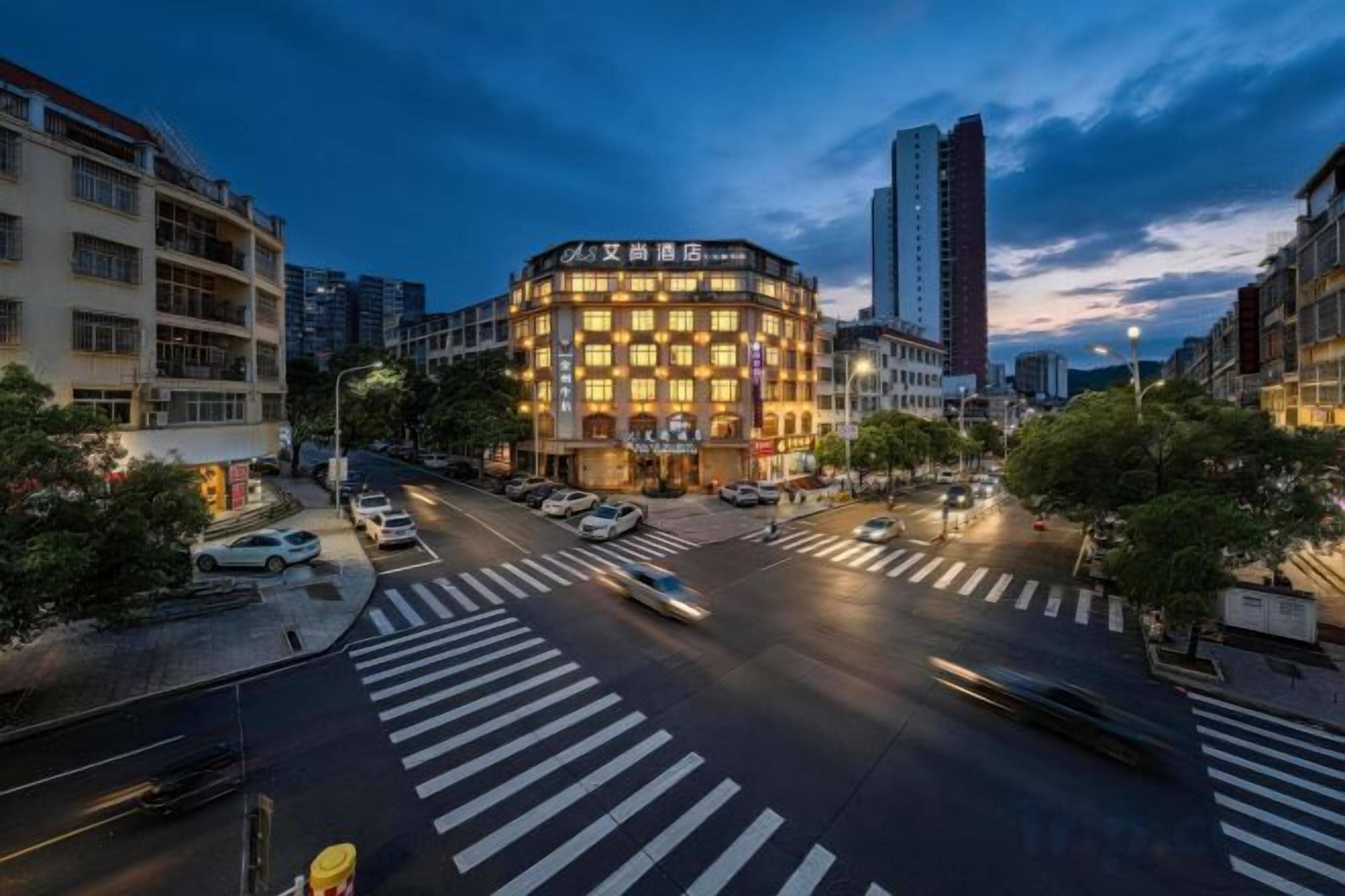 A multi-story hotel with a distinctive corner design, a pedestrian crossing, and a busy urban street.