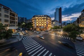 A multi-story hotel with a distinctive corner design, a pedestrian crossing, and a busy urban street. - Aishang Hotel (Pubei Maoyuan Diwang International) (Pubei)