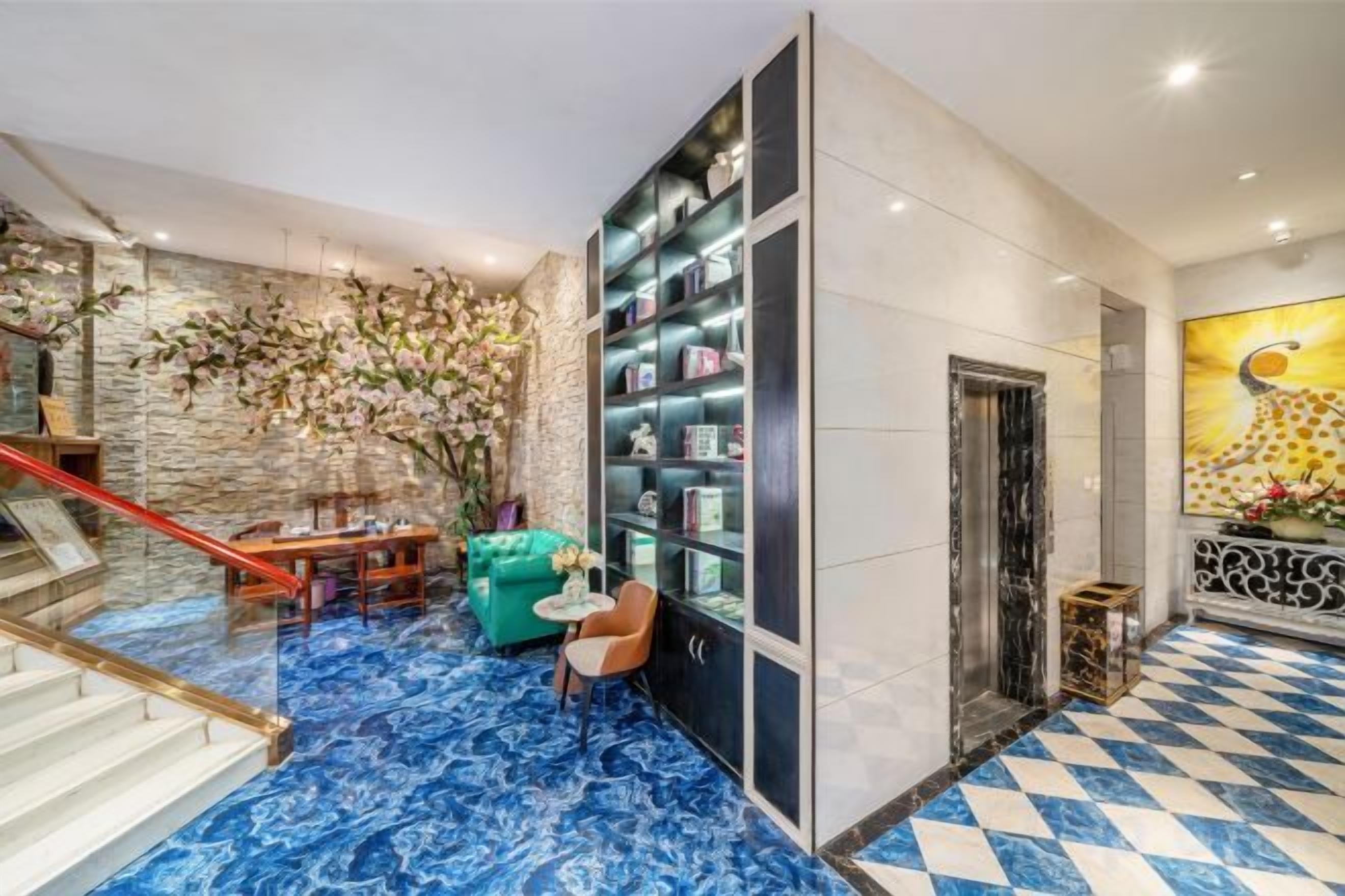 A lobby with a marble floor, a staircase, a green sofa, a bookshelf, and a large painting.