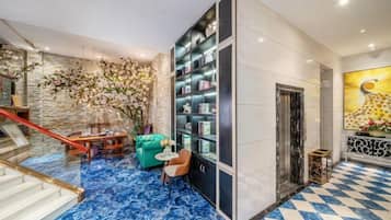 A lobby with a marble floor, a staircase, a green sofa, a bookshelf, and a large painting.