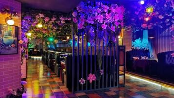 A bar area with a checkered floor, a black partition with flowers, and hanging floral decorations.