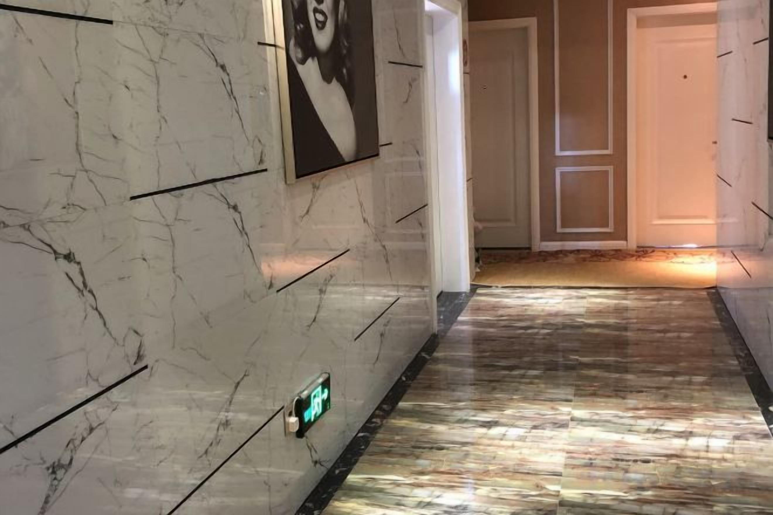 A hallway with marble walls and a patterned floor, leading to a door.