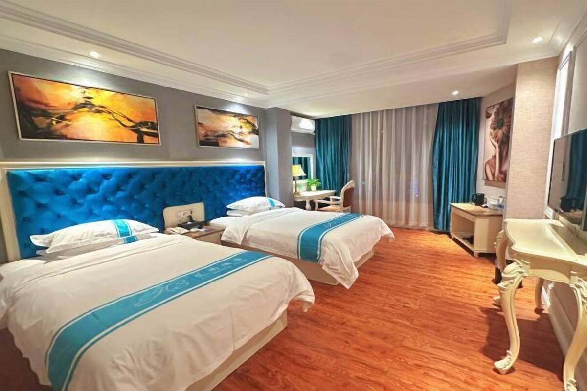 Quarto de hotel com duas camas, uma escrivaninha, uma cadeira e obras de arte nas paredes.