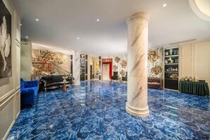 Un hall d’entrée spacieux avec un sol en marbre, une grande colonne, un canapé et un comptoir d’accueil.