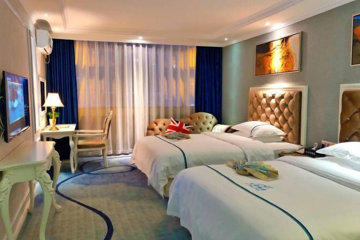 Quarto de hotel com duas camas, uma escrivaninha, uma cadeira e uma televisão.