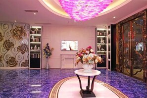A lobby with a marble floor, a central table with a floral arrangement, and a television screen on the wall. - Aishang Hotel (Pubei Maoyuan Diwang International) (Pubei)