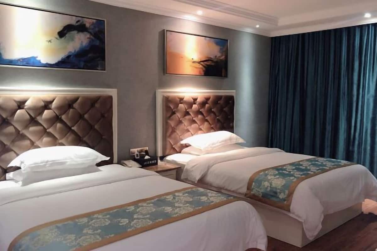 A hotel room with two beds, each with a tufted headboard, a large painting above the beds, and a blue curtain on the right.