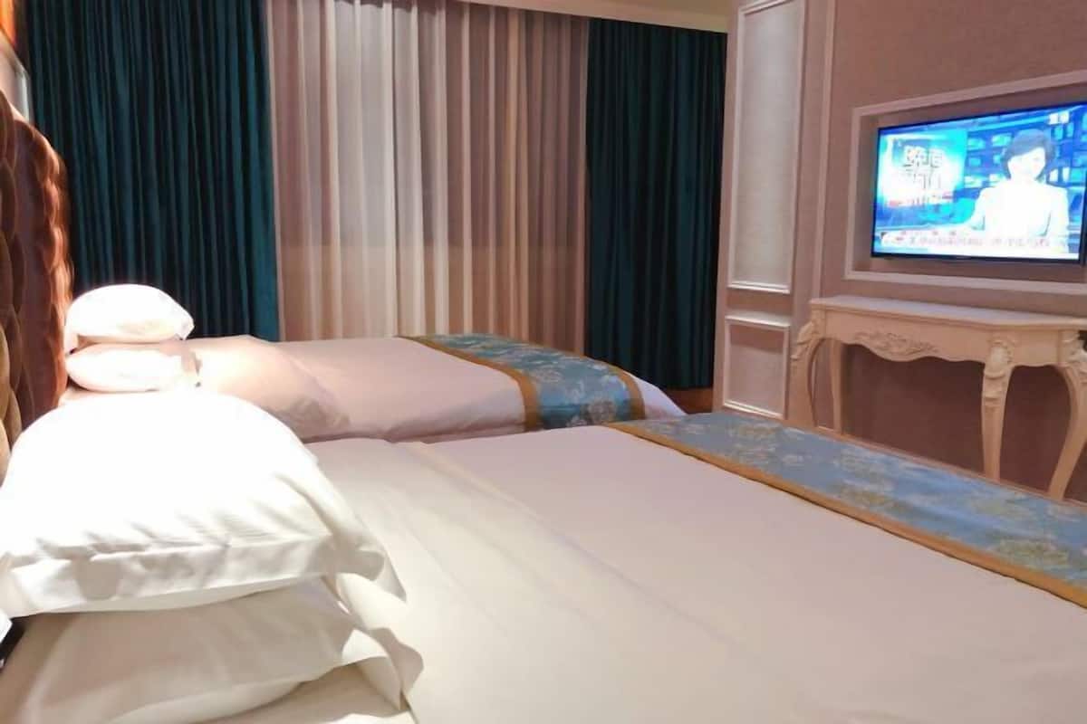 A hotel room with two beds, a television on the wall, and a curtain backdrop.