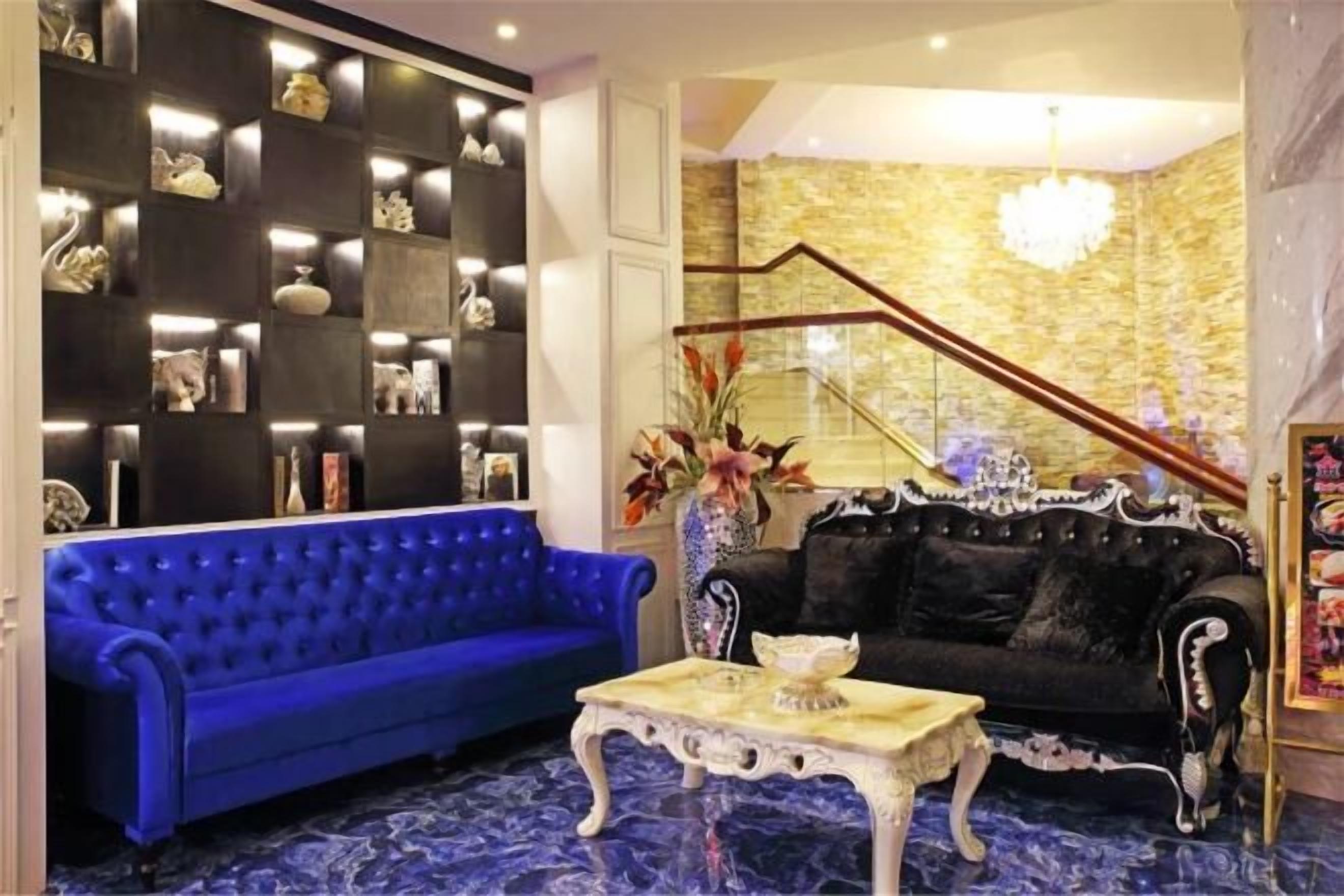 A room with a blue sofa, a black sofa, a white coffee table, and a staircase with a golden railing.