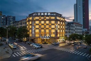 A multi-story hotel with a corner entrance, a visible storefront, and a parking lot with cars. - Aishang Hotel (Pubei Maoyuan Diwang International) (Pubei)