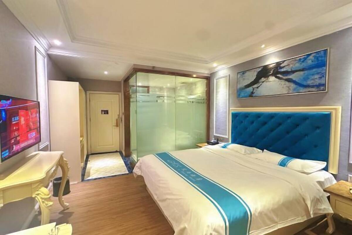 Quarto de hotel com cama grande, televisão, armário de portas de vidro e um quadro na parede.
