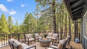A deck with outdoor furniture and a fire pit, surrounded by trees. - Comfortable Chic | Hot Tub | AC | MTN View (Flagstaff)