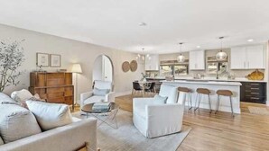A modern living room with a sofa, armchair, and coffee table. There is a kitchen area with a dining table and bar stools. - Comfortable Chic | Hot Tub | AC | MTN View (Flagstaff)