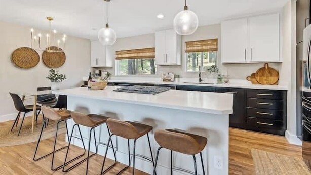 A modern kitchen with a central island, bar stools, pendant lighting, and white cabinetry. - Comfortable Chic | Hot Tub | AC | MTN View (Flagstaff)