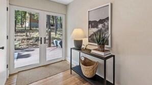 A room with a sliding glass door leading to an outdoor area, a small table with a lamp, a framed picture on the wall, and a basket on the floor. - Comfortable Chic | Hot Tub | AC | MTN View (Flagstaff)