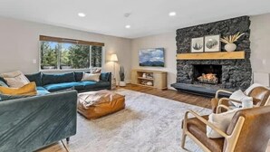 A modern living room with a stone fireplace, a blue sofa, and a leather armchair. - Comfortable Chic | Hot Tub | AC | MTN View (Flagstaff)