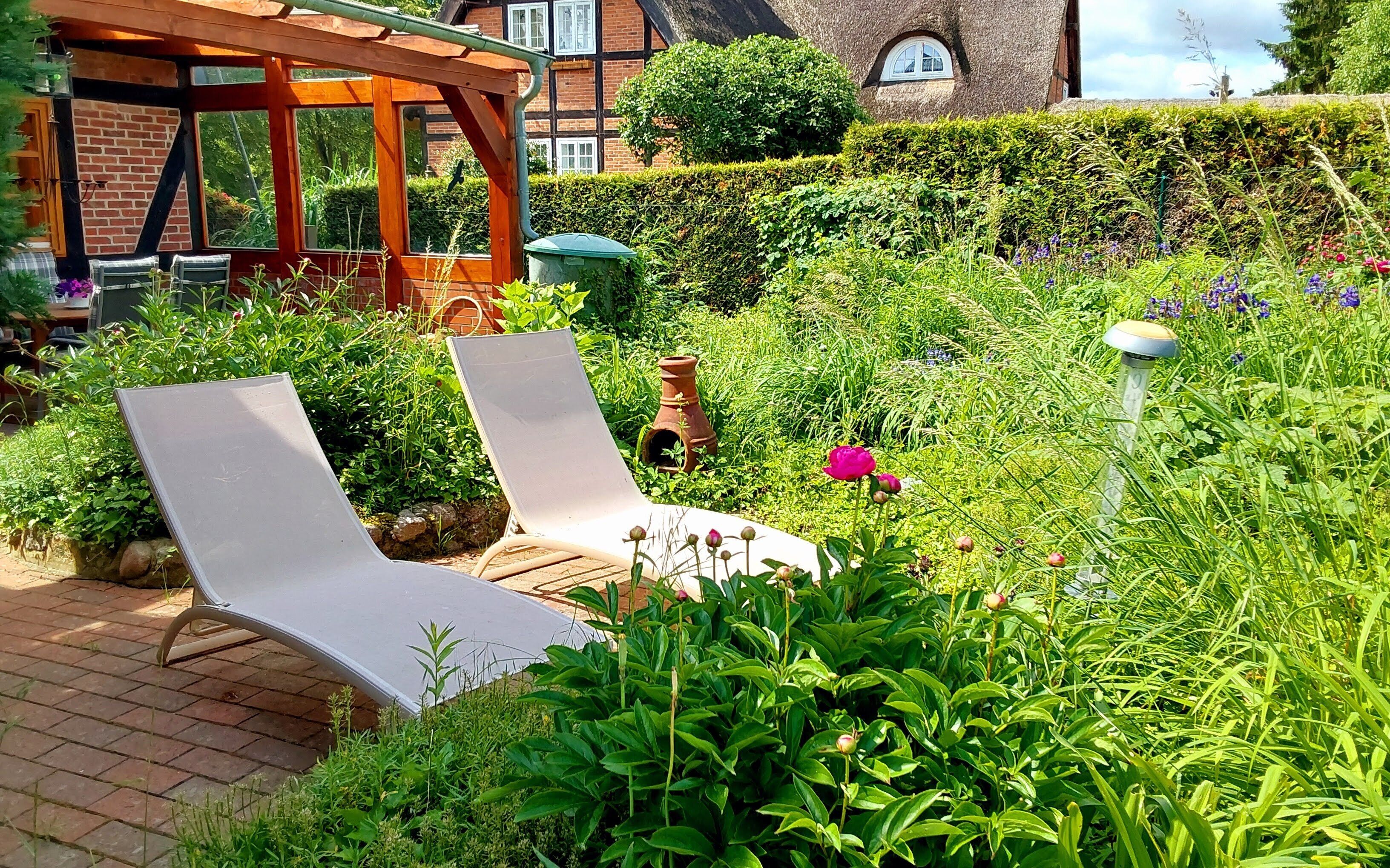 A garden with two lounge chairs, a brick pathway, and a brick building in the background.