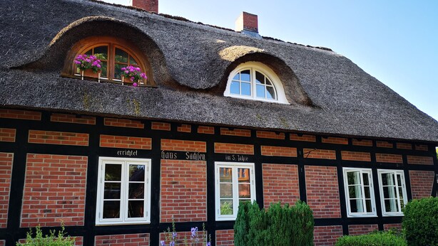 Un edificio tradizionale in mattoni con tetto di paglia, numerose finestre e un giardino ricco di piante e fiori.