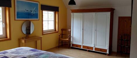 A bedroom with a bed, a wardrobe, a desk, a chair, and a painting on the wall.