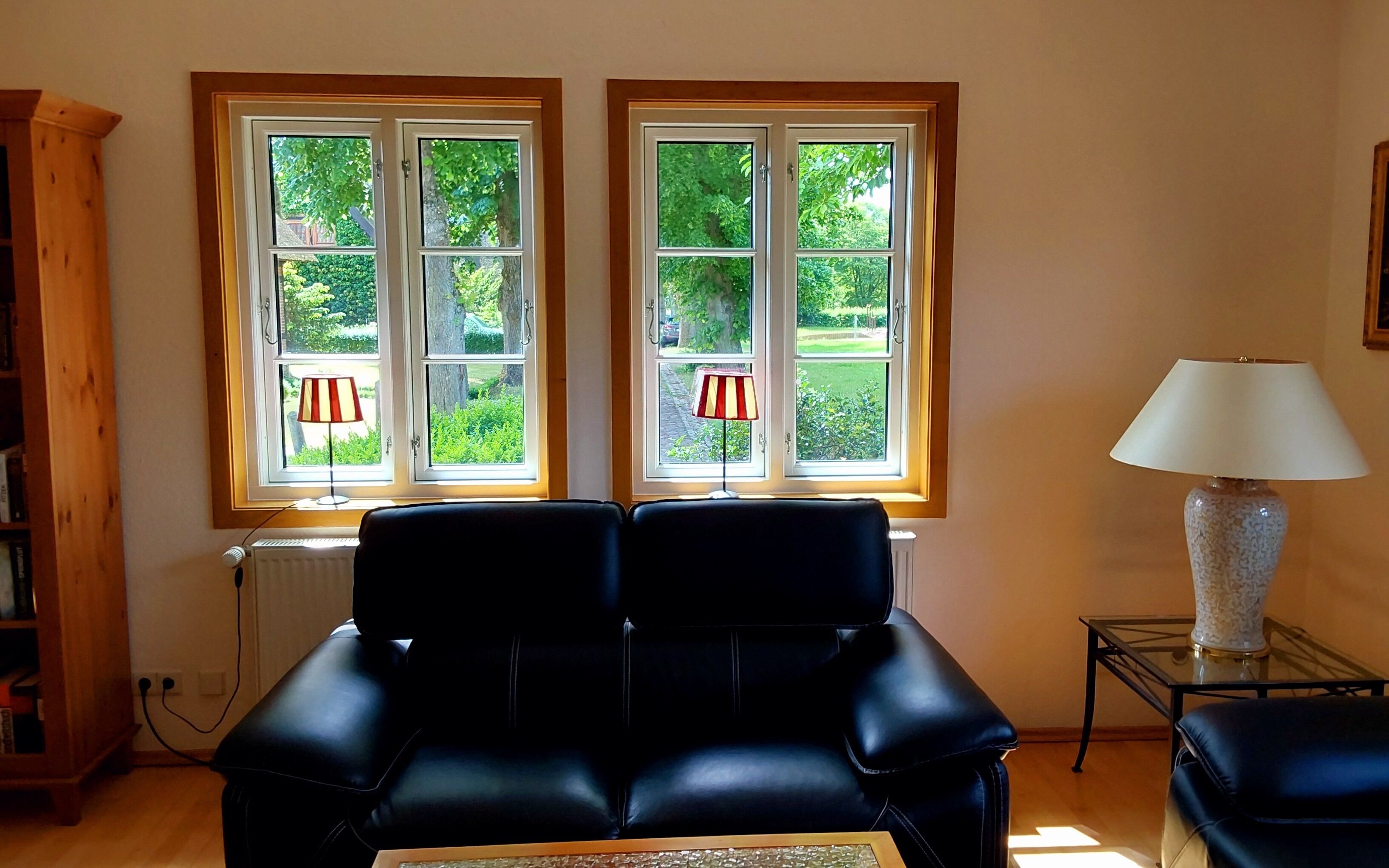 A room with two black leather sofas, a radiator, a lamp, and a window with a view of greenery.