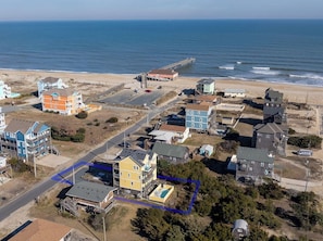 An aerial view of a coastal residential area with houses, a pier, and a beach.