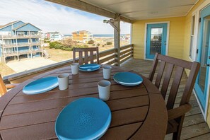 A wooden deck with a table set for four, overlooking a beach with buildings in the background.