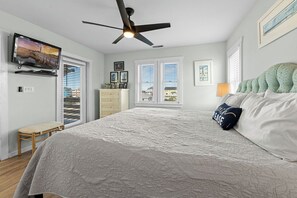 Un dormitorio con cama, ventilador de techo, televisor y ventana con persianas.