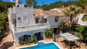 Eine zweistöckige Villa mit Schwimmbad, Außenbereich mit Sitzgelegenheiten und einer überdachten Terrasse.