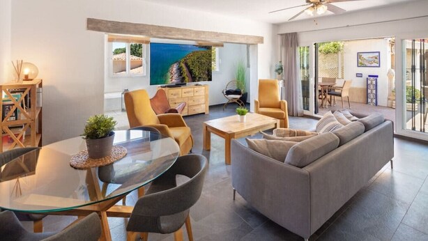 Ein modernes Wohnzimmer mit einem Glastisch, bequemen Sitzgelegenheiten, einer Couch und einem Deckenventilator.