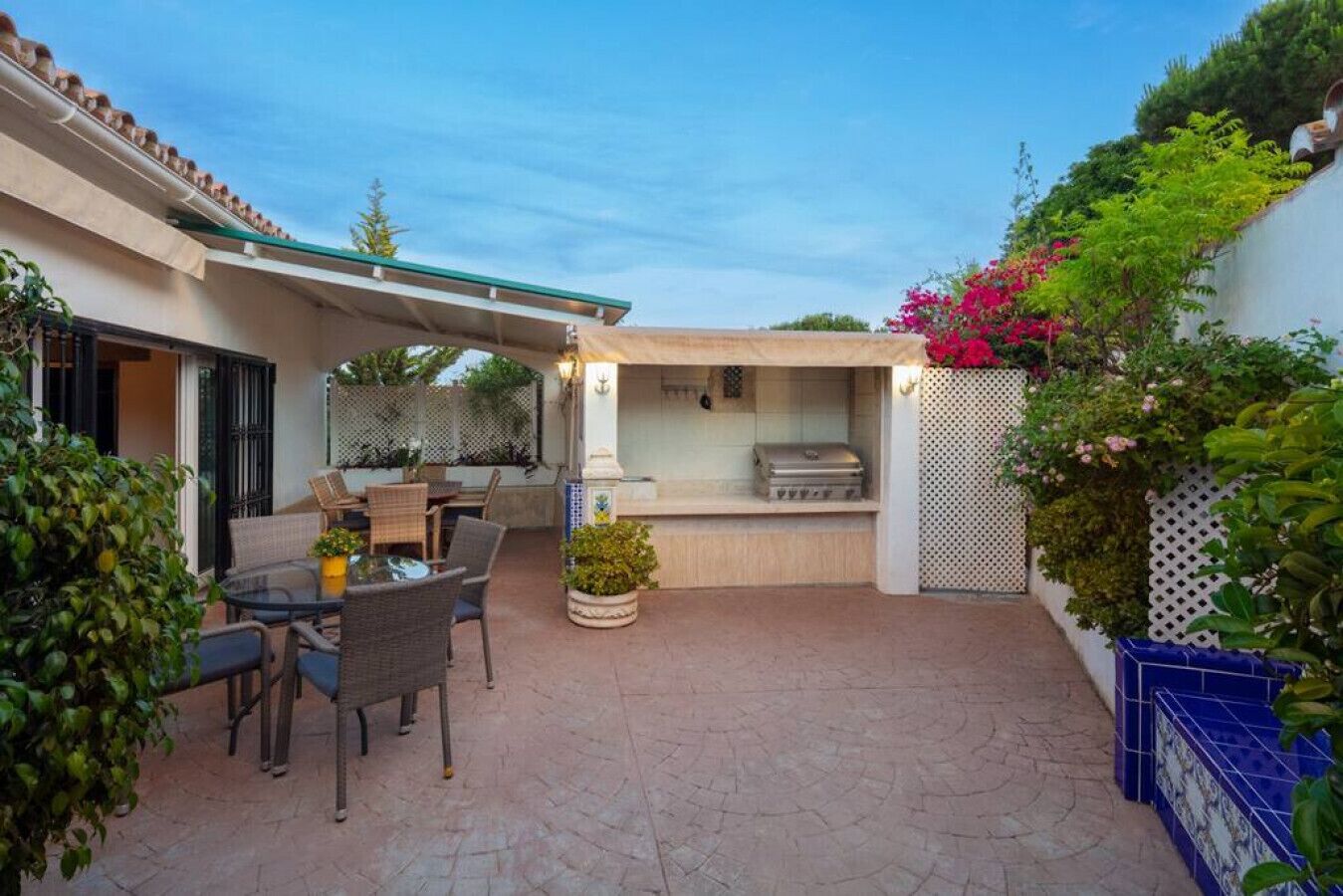 A patio area with a dining table and chairs, a barbecue grill, and potted plants.