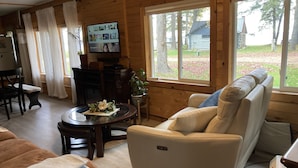 A cozy cabin interior with a sofa, a coffee table, a TV, and a view of the outside. - 4 seasons of adventures on Indian Lake/Sunset View Resort/Unit#4 (Manistique)