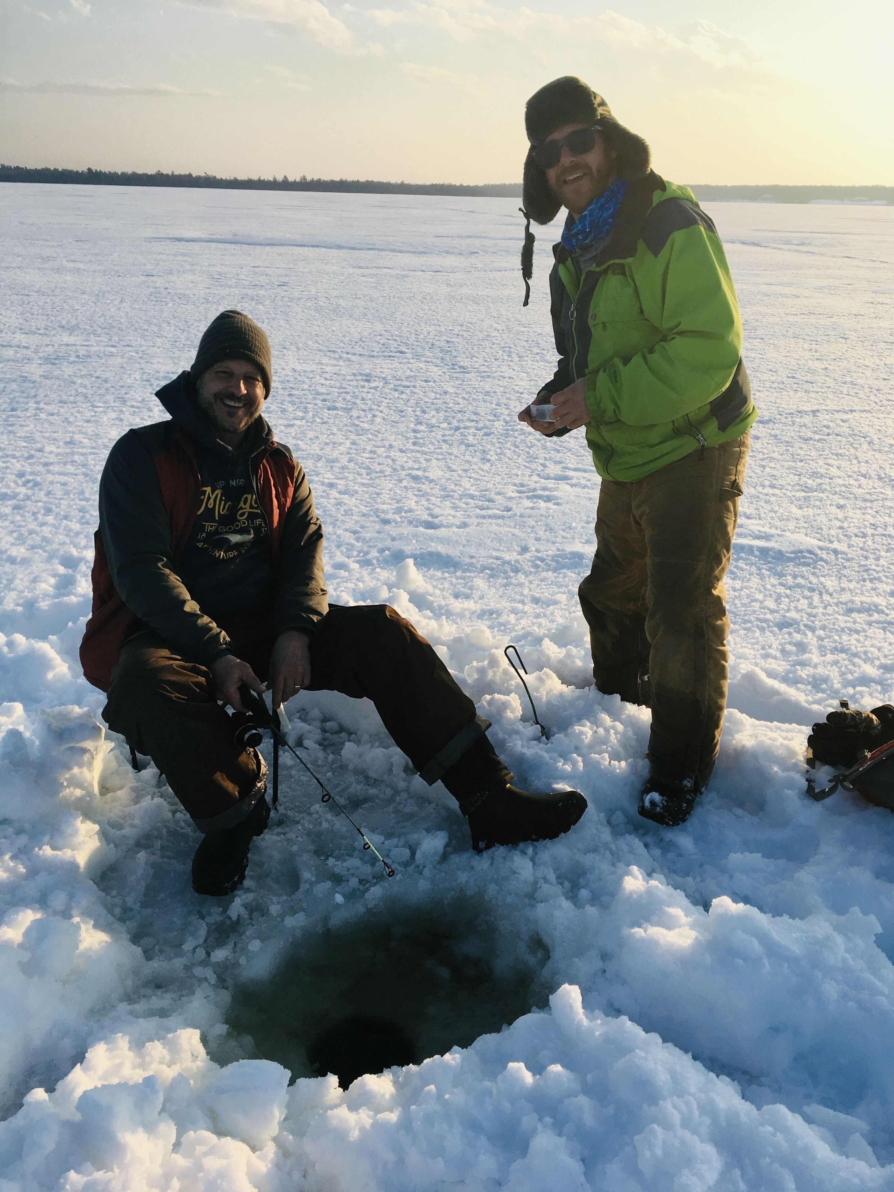 Deux personnes sont en train de pêcher sur un lac gelé, entouré de neige.