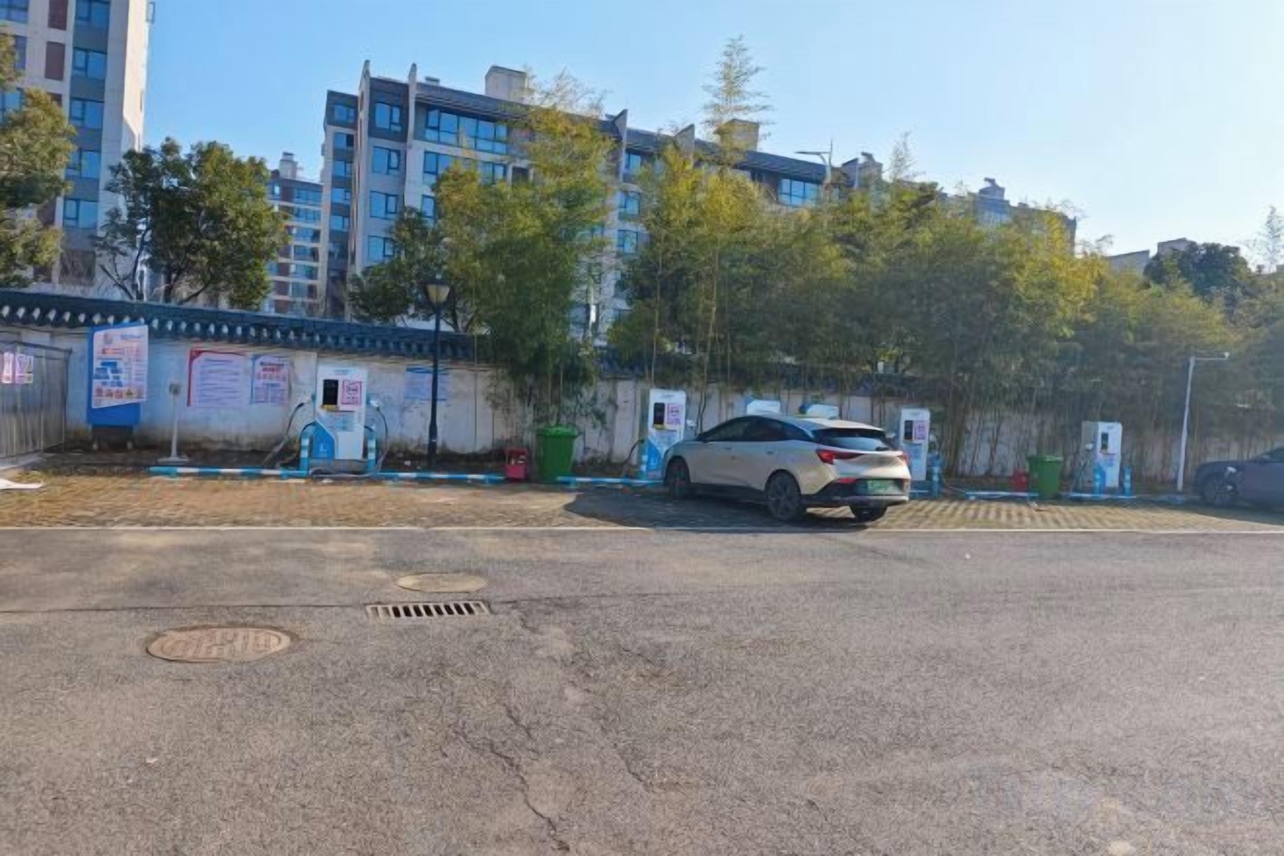 A parking lot with a white car parked near a building with multiple floors and a blue fence.