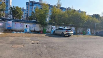 A parking lot with a white car parked near a building with multiple floors and a blue fence.