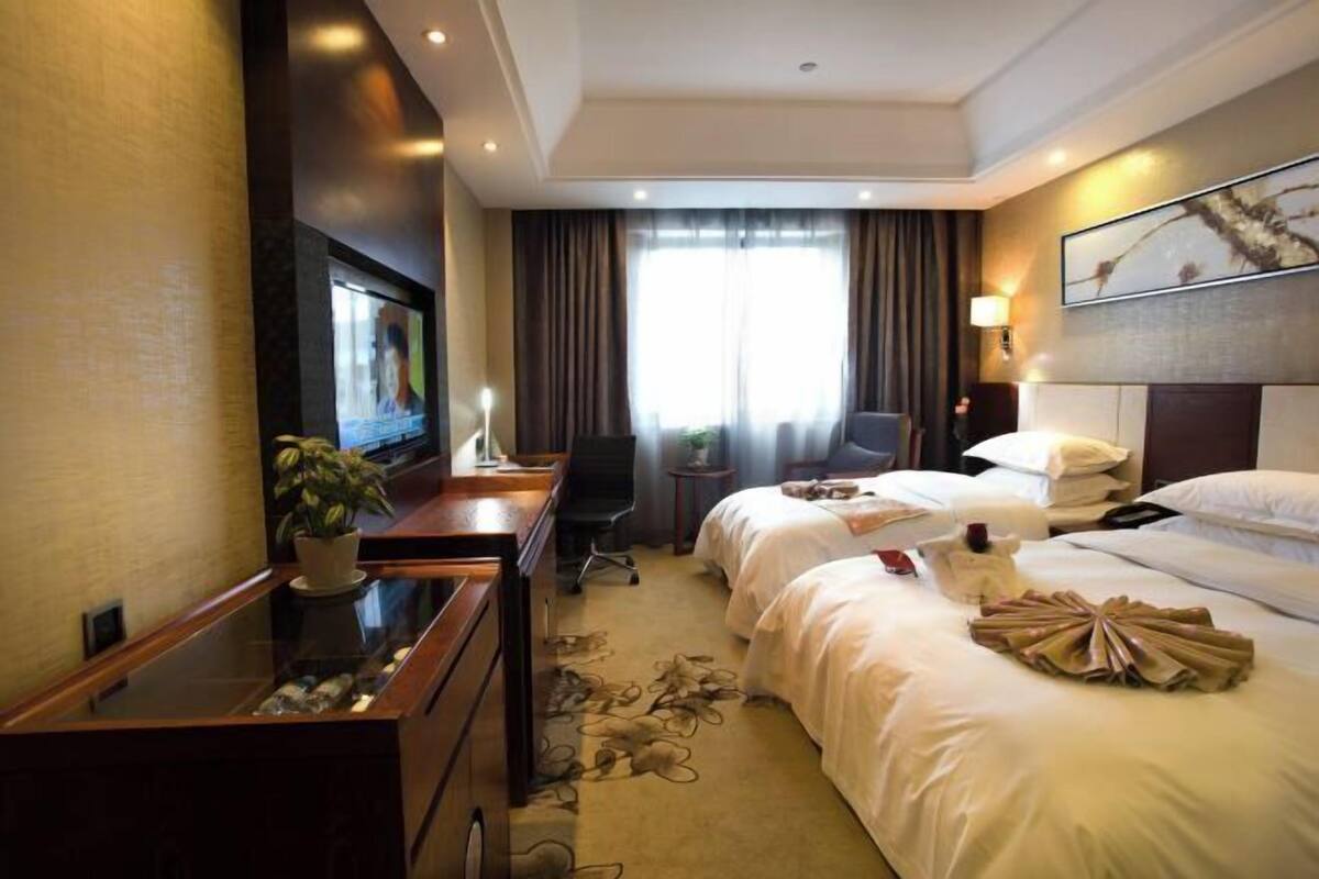 A hotel room with a bed, a desk, a chair, a TV, and a window with curtains.