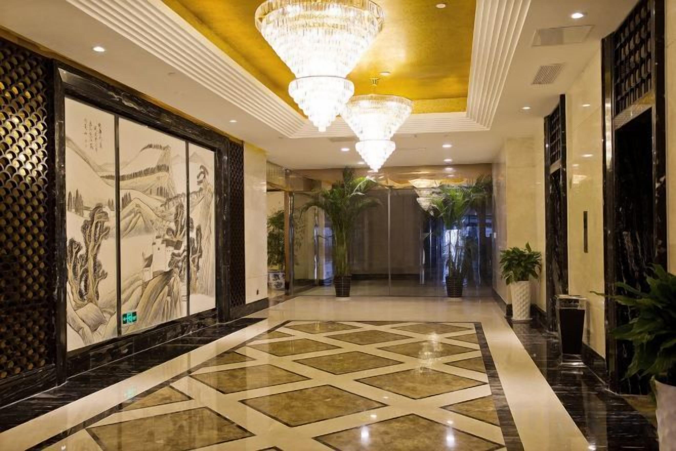 Un'accogliente hall d'hotel con pavimento decorato, grandi lampadari e un'opera d'arte tradizionale alle pareti.