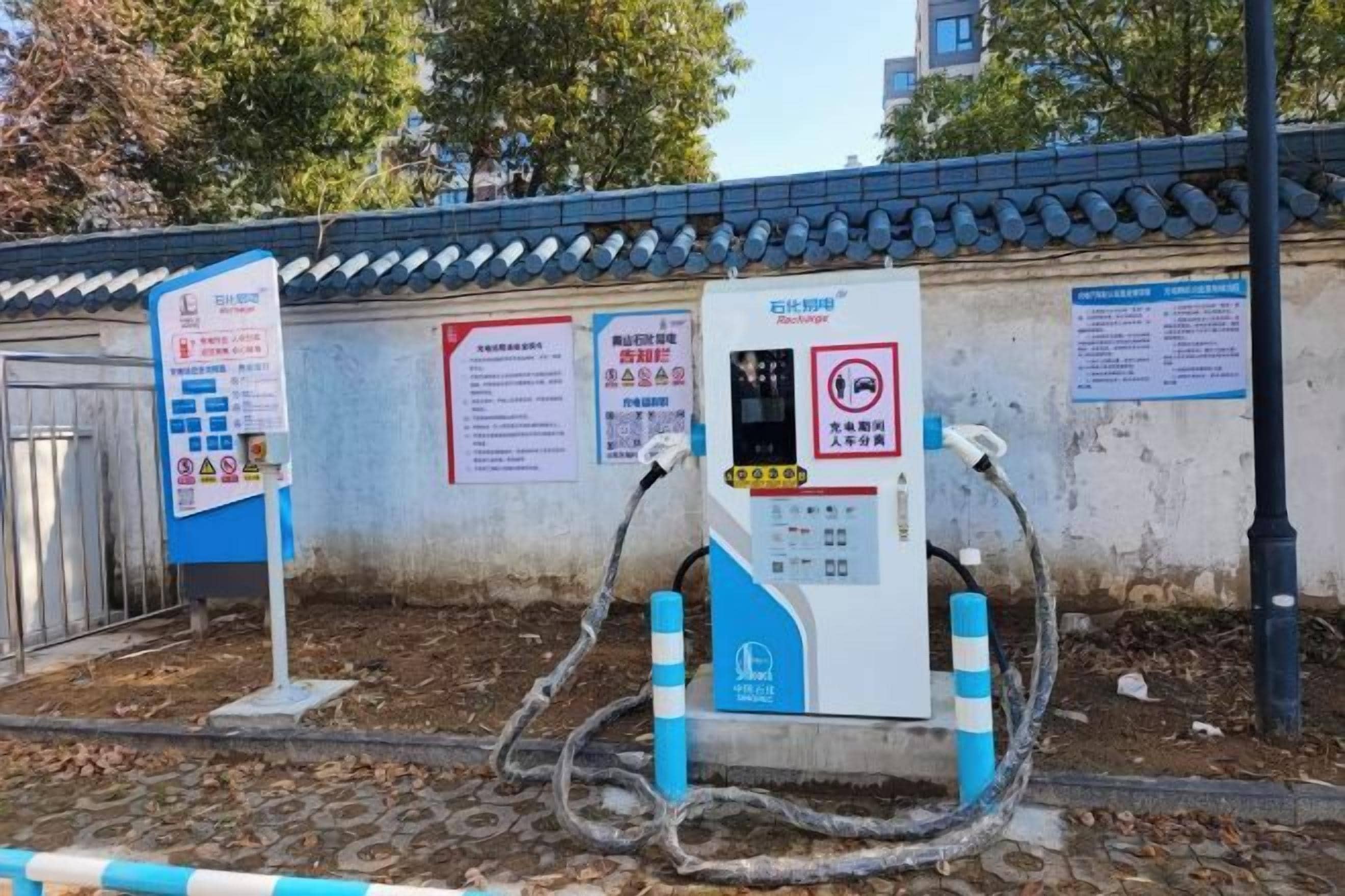 A portable electric vehicle charging station with multiple cables connected to it, situated outdoors with a tiled wall and signage in the background.